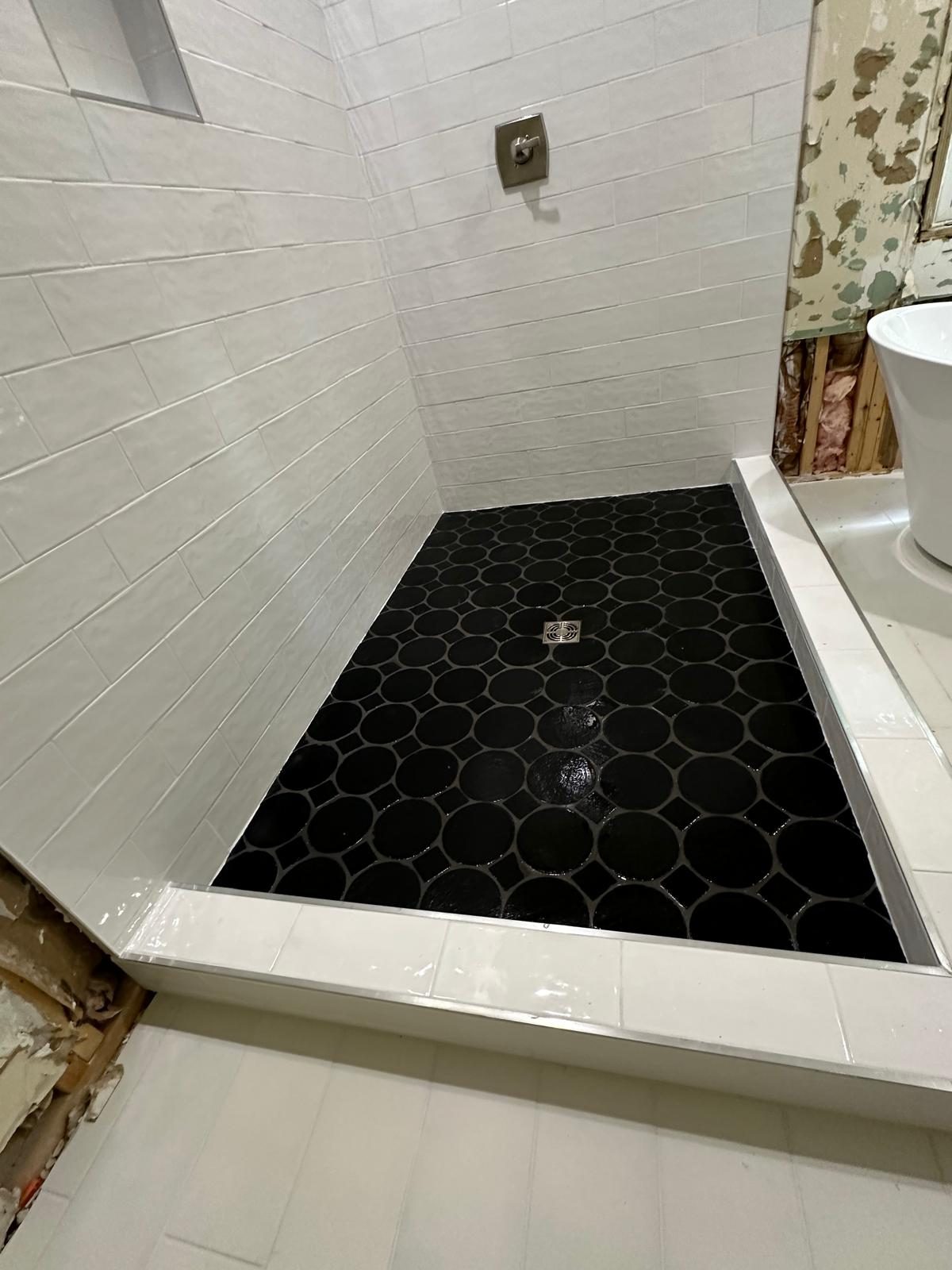 White subway tile shower with black penny round mosaic floor